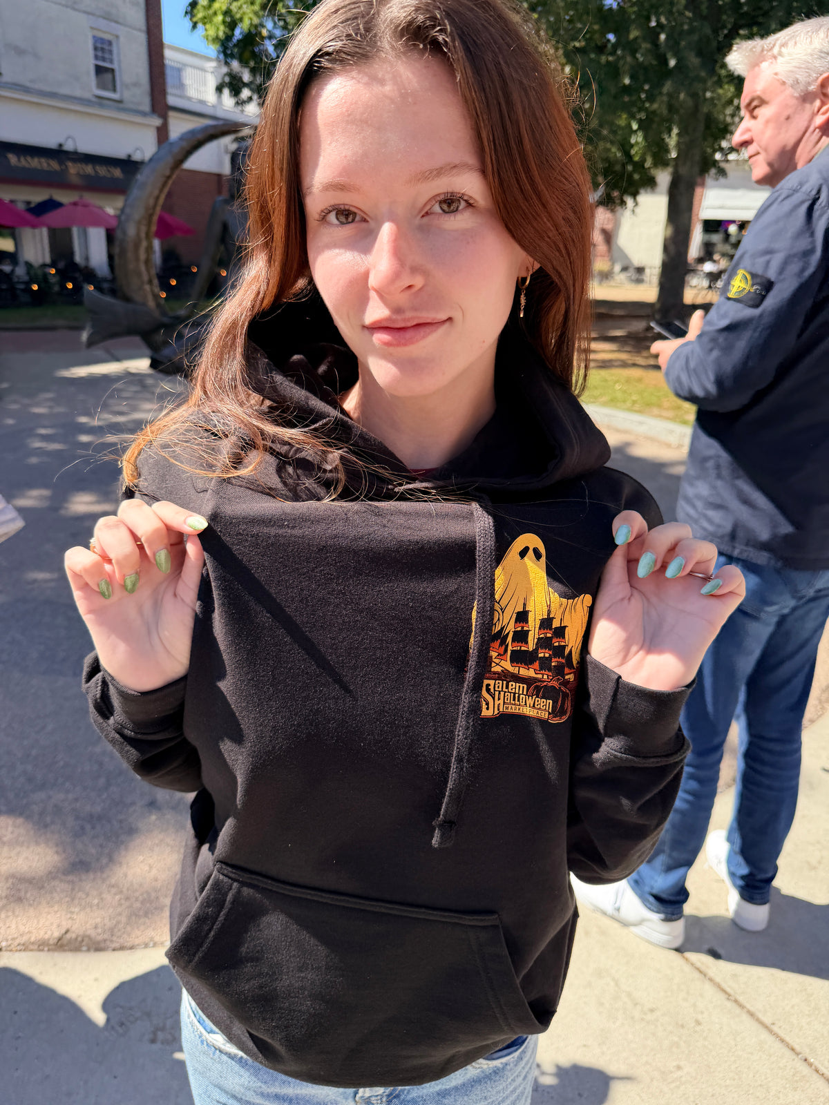 Close view of the gold ghost and sailing ship artwork on the left chest of the 2026 black hooded sweatshirt.