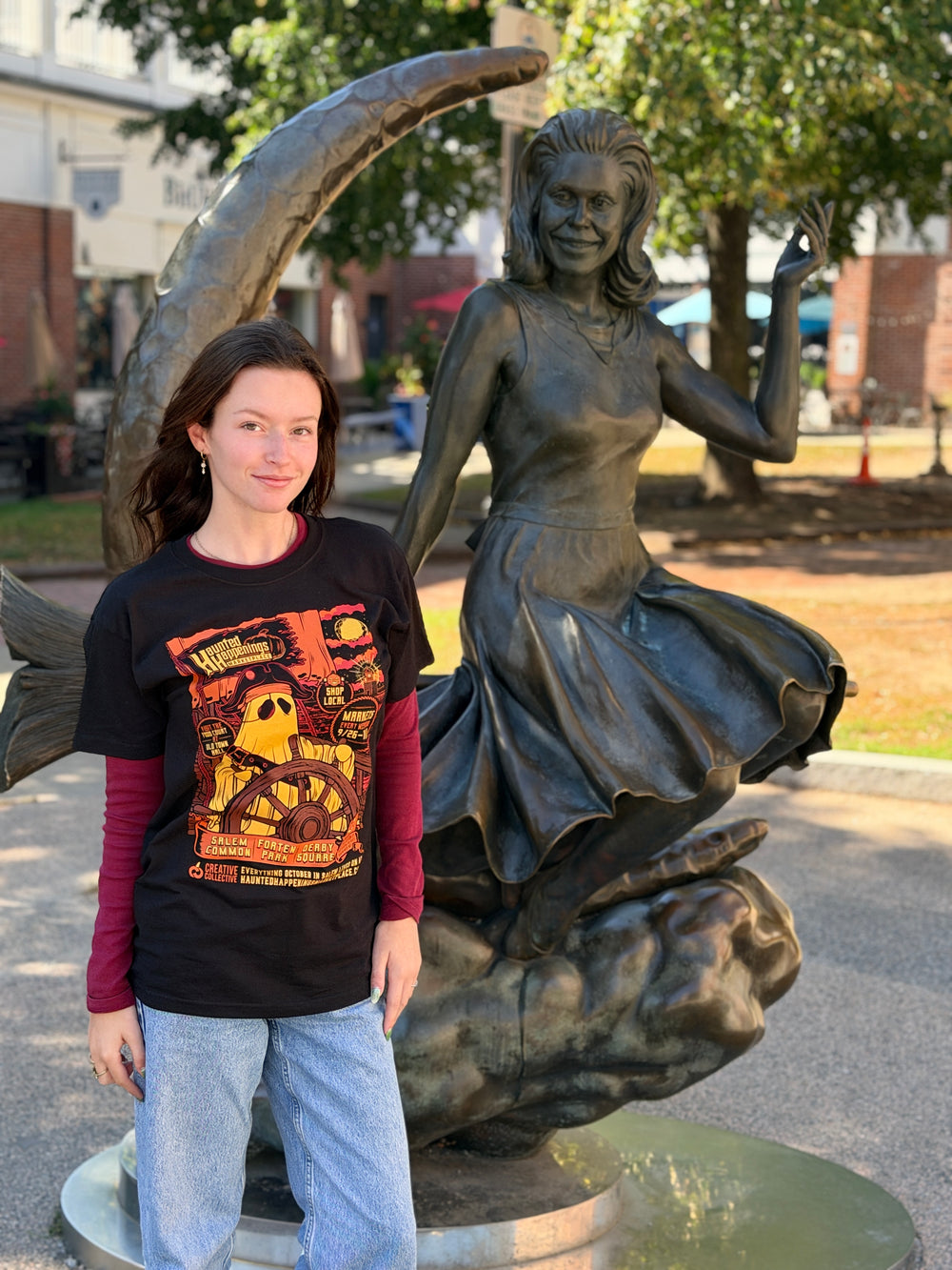Model wearing the black 2026 Pirate Ghost T-shirt beside the Bewitched statue in Salem.