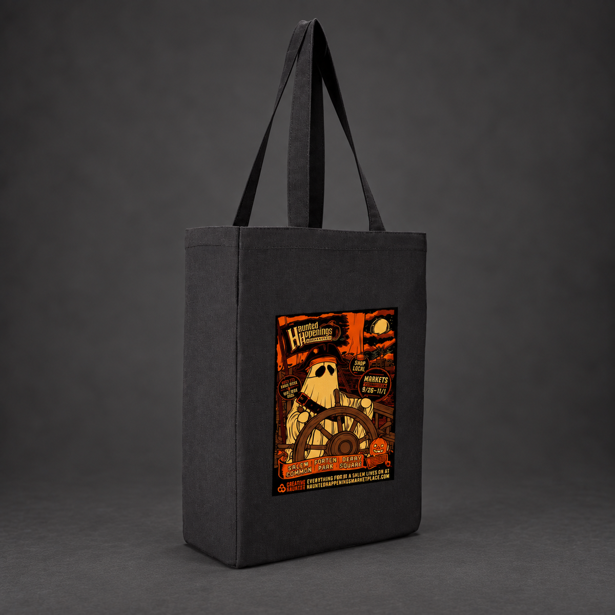 Mockup of a black Pirate Ghost canvas tote with orange and gold artwork against a charcoal background.