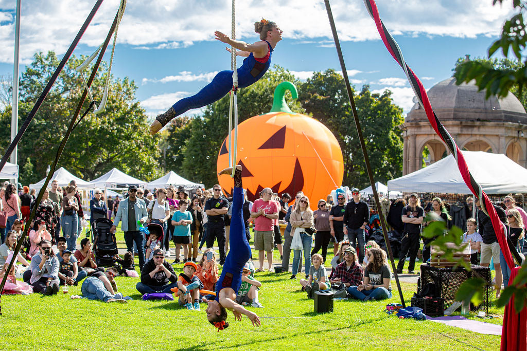 Crowds watching aerial performers beside a giant pumpkin at Salem Common